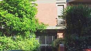 Un edifici de diversos pisos amb façana de maó, balcons amb plantes i una entrada tancada per una reixa.