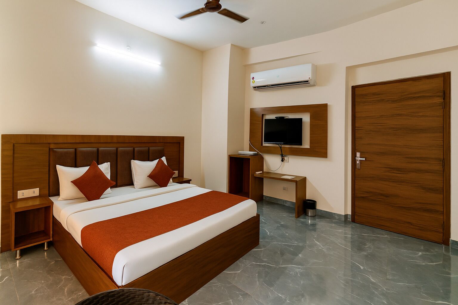Ein Hotelzimmer mit Bett, Schreibtisch, Fernseher, Klimaanlage und einer Tür.