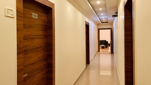 A modern hotel hallway with wooden doors, a tiled floor, and recessed ceiling lighting. - Hotel Yash Regency - Managed by JMD Group (New Delhi)