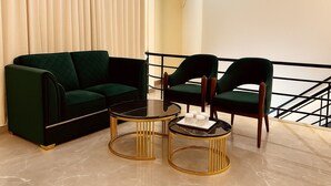 A modern living area with a green sofa, two matching chairs, and a glass coffee table with gold accents. - Hotel Yash Regency - Managed by JMD Group (New Delhi)