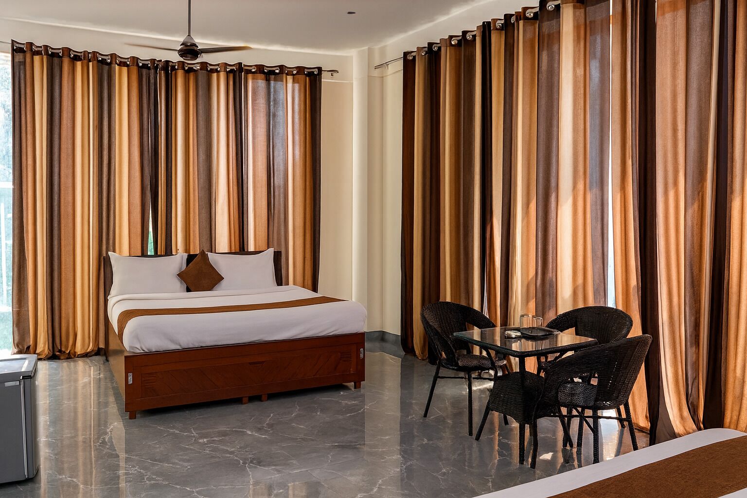 A hotel room with a bed, a dining table with chairs, and curtains.