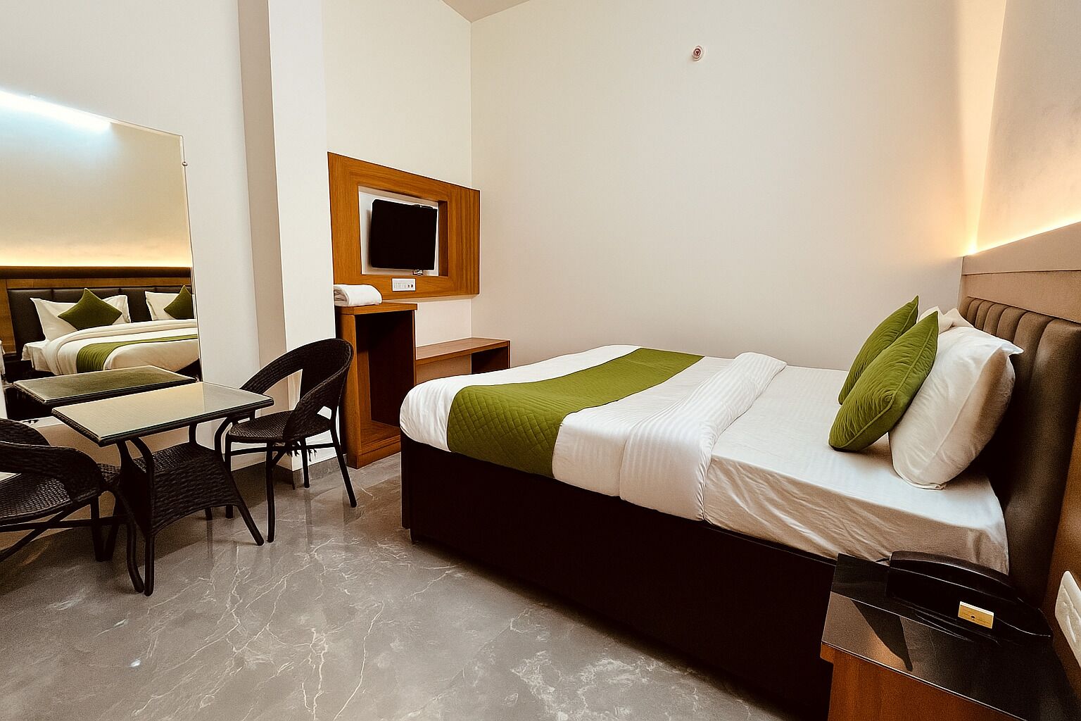 A hotel room with a bed, a desk, a chair, a small table, and a TV mounted on the wall.