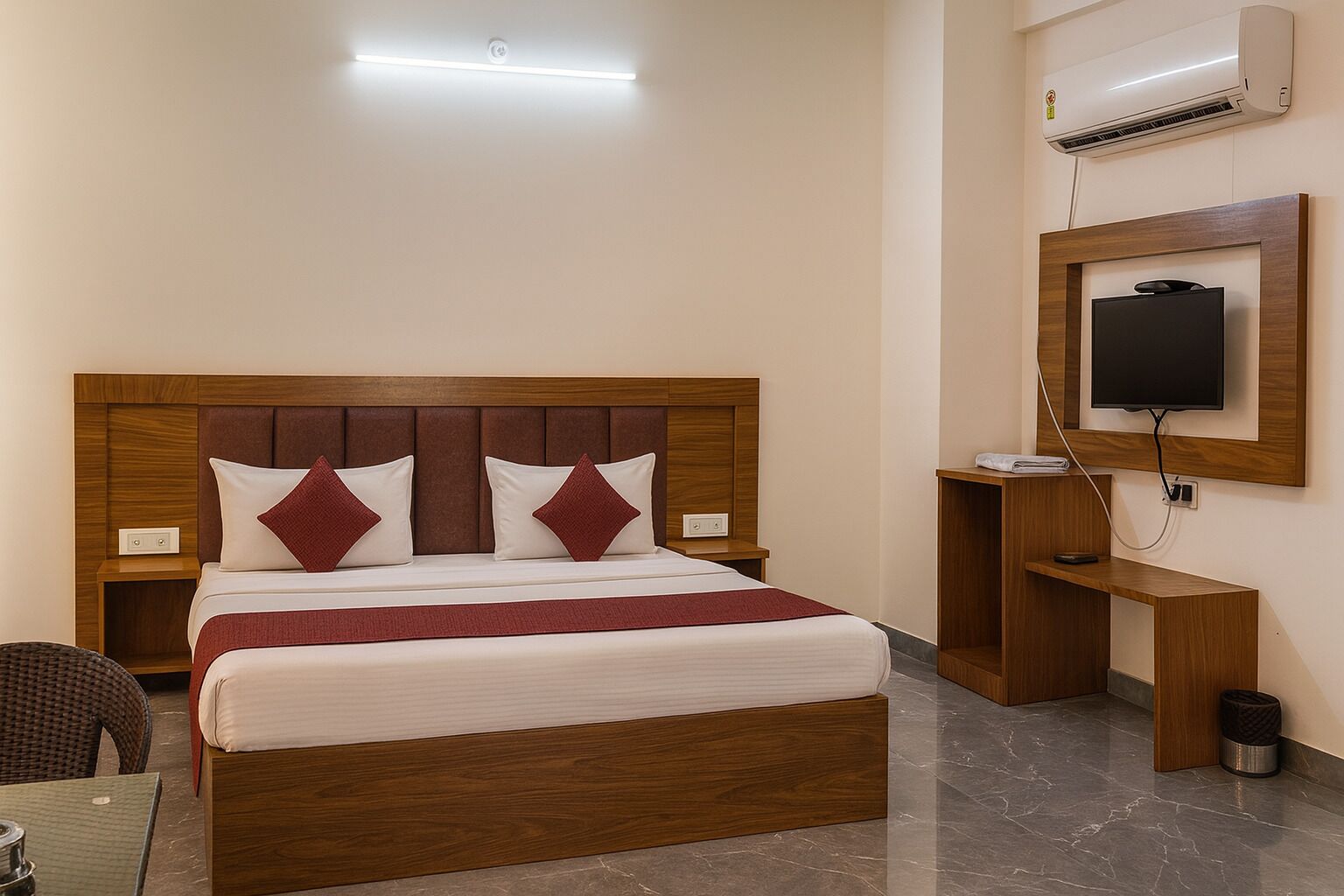 Een hotelkamer met een houten bed, een aan de muur bevestigde televisie, een klein bureau en een airconditioning.