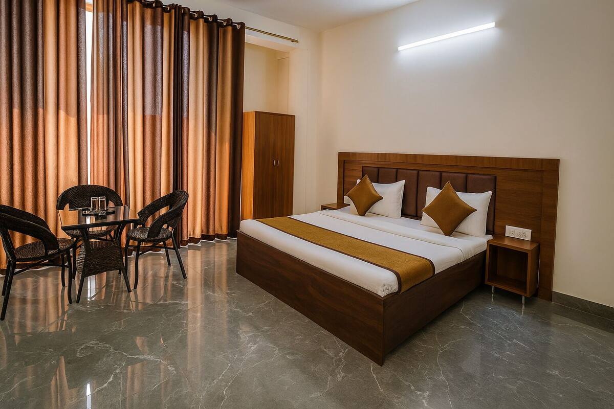 A hotel room with a large bed, a wooden headboard, a bedside table, a chair, a small table with a glass, and a curtain.