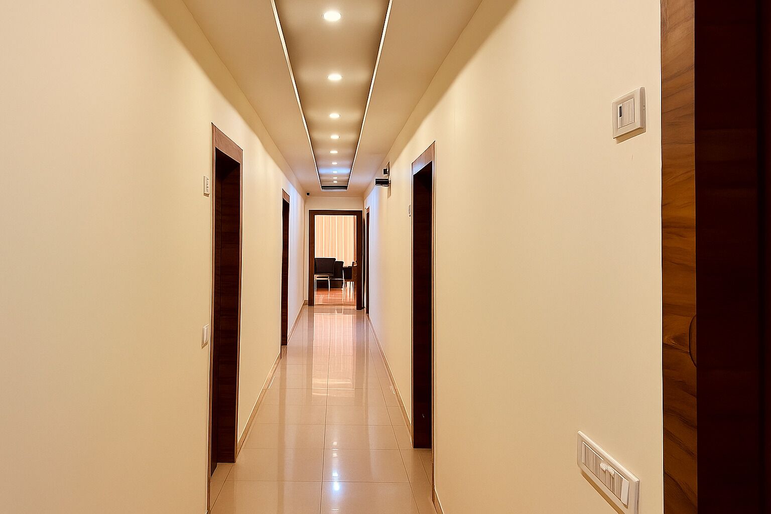 A hotel hallway with a modern design, featuring a long corridor with doors on both sides, a tiled floor, and recessed ceiling lighting.