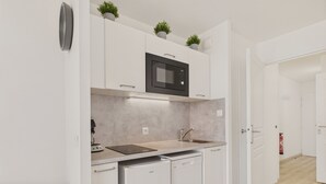 Une cuisine moderne avec des meubles blancs, un four à micro-ondes encastré, un évier et un lave-vaisselle. On peut voir des plantes en pot sur le plan de travail et une poubelle à gauche.