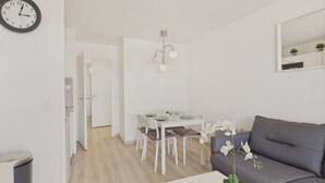 Un salon moderne avec un canapé gris, une table basse blanche agrémentée d’une plante, et un coin repas avec des chaises et une table blanches.