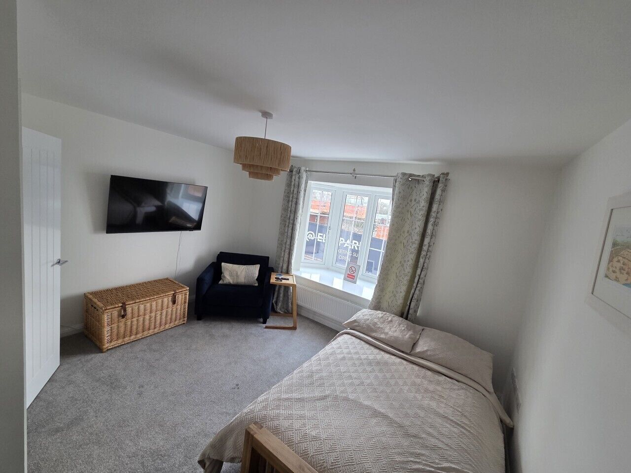 A bedroom with a bed, a TV, a chair, a small table, and a window with curtains.
