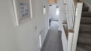 En hall med en trappa, en inramad skylt på väggen och en hängande lampa.