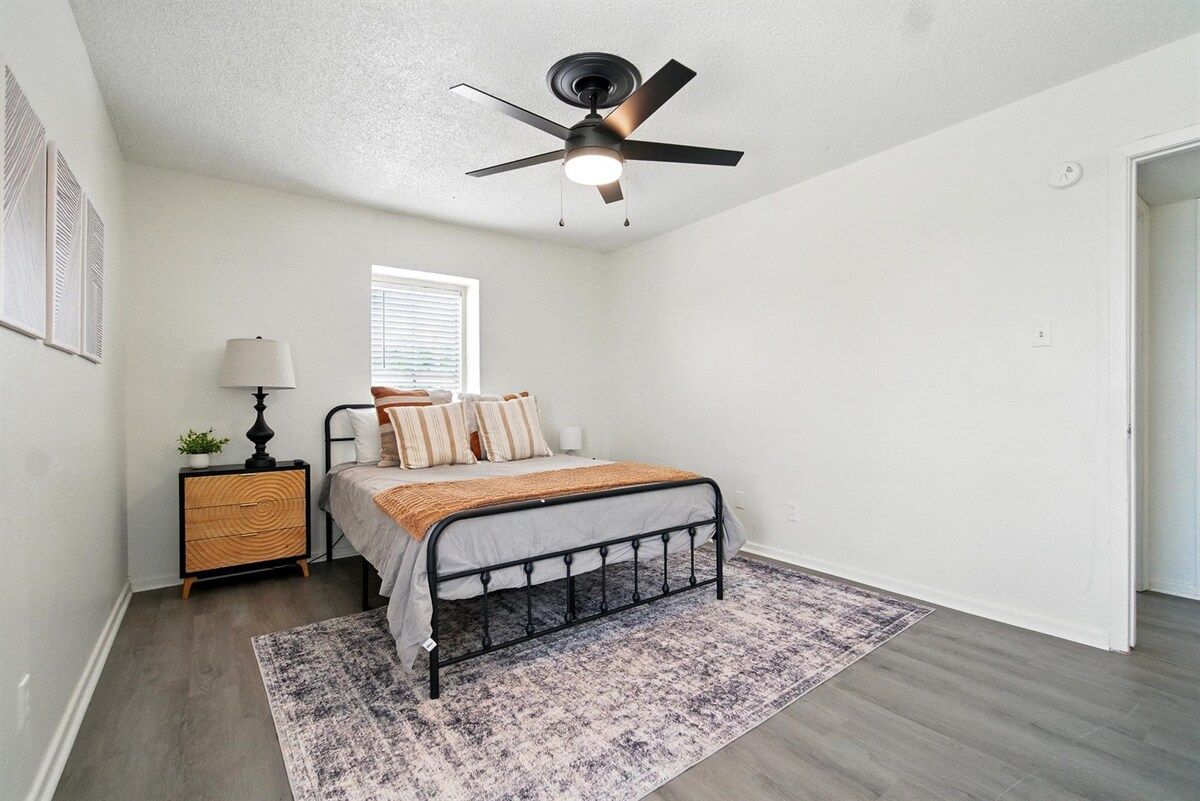 A bedroom with a bed, a nightstand, a lamp, a ceiling fan, and a window.