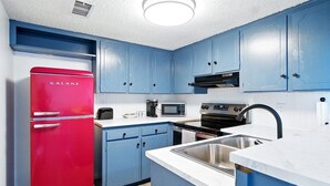 Una cocina con armarios azules, un refrigerador rojo, un microondas, una estufa y un lavamanos.