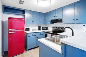 A kitchen with blue cabinets, a red refrigerator, a microwave, a stove, and a sink. - Radford Collection Eight: Abilene Heights (Abilene)