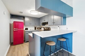 A compact kitchen with a red refrigerator, a microwave, and a sink. There are two stools at a bar counter.