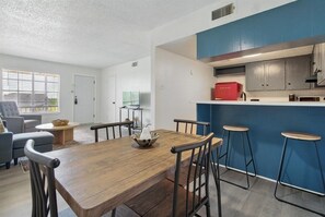 A modern living room with a wooden dining table, grey sofa, and a kitchen area with blue cabinets and a red appliance. - Radford Collection Eight: Abilene Heights (Abilene)