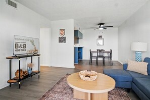A modern living room with a round wooden coffee table, a blue sofa, and a dining area with a table and chairs. - Radford Collection Eight: Abilene Heights (Abilene)