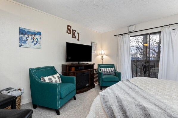 A hotel room with a bed, two teal armchairs, a television, and a ski-themed wall.