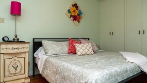 Een slaapkamer met een bed, nachtkastje, lamp en bloemrijk kunstwerk aan de muur.