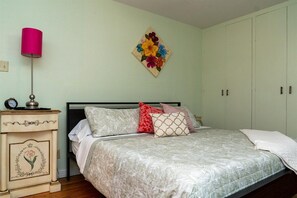 Une chambre à coucher comprenant un lit, une table de chevet, une lampe et une œuvre d’art florale accrochée au mur.