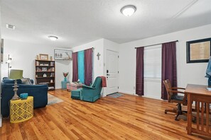 A living room with a sofa, armchair, and a small table. There is a bookshelf with books and a framed welcome sign.