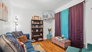 Een woonkamer met een blauwe bank, een boekenkast, een kleine tafel met een vaas, en een bordje met de tekst 'WELCOME HOME B&B HOSTING'.