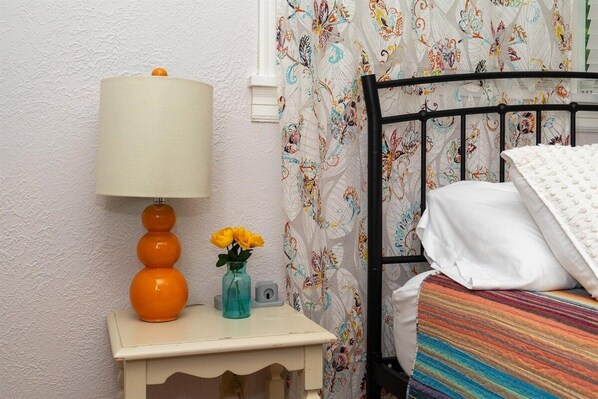A bedroom with a bed, a nightstand with a lamp, and a vase with flowers.