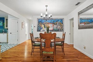 Comedor con mesa y sillas de madera, candelabro y un cuadro grande en la pared.
