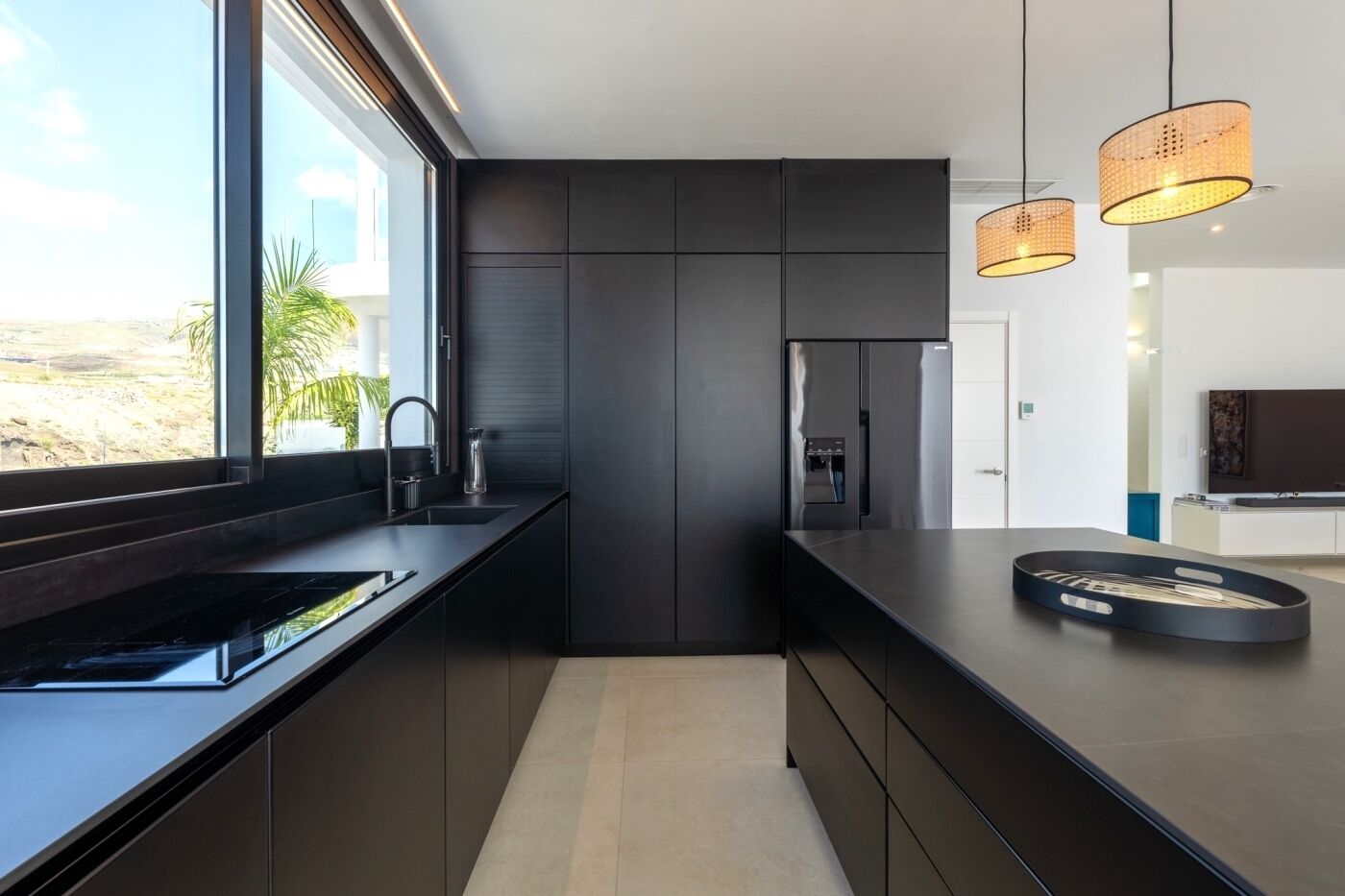 Een moderne keuken met donkere kastjes, een groot raam en een inbouwkoelkast.