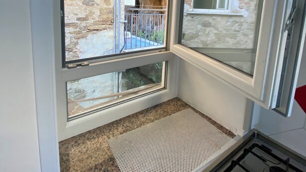 A kitchen with a gas stove, a window overlooking a stone wall and a small balcony.