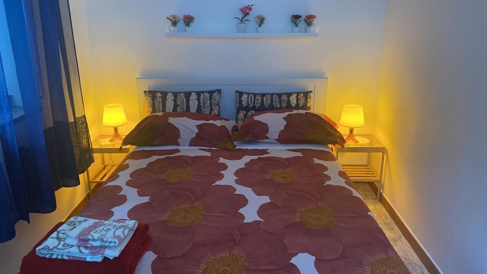Una camera da letto con un letto grande, due lampade sui comodini, un tavolino e uno scaffale con fiori.