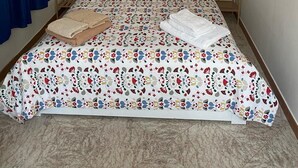 A neatly made bed with floral bedding, two bedside tables with lamps, a blue curtain, and a wall-mounted shelf with flowers.