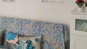 A room with a patterned sofa, three framed artworks, and a small table with potted plants.