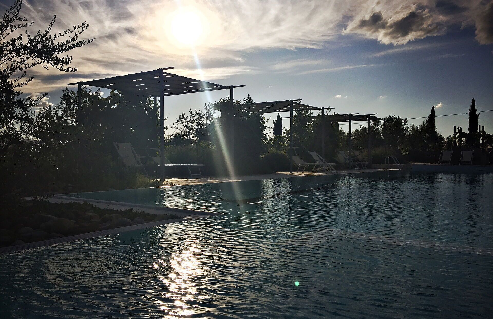 Una piscina con rayos de sol, una pérgola y sillones de descanso.