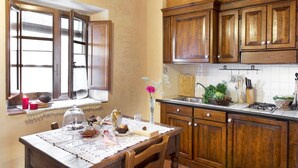 Una cocina con armarios de madera, una ventana con cortinas y una mesa con mantel de encaje, además de varios utensilios de cocina.