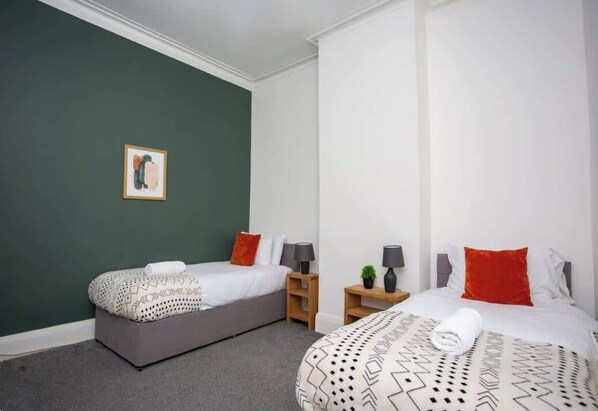 Habitación de hotel con dos camas, una pared de acento verde y un cuadro enmarcado.