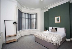 Ein Schlafzimmer mit einem Bett, einem Fenster mit Jalousien, einem Heizkörper und einem gerahmten Bild an der Wand.
