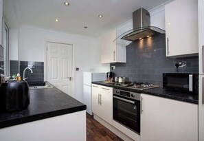 A modern kitchen with white cabinets, a black countertop, a stainless steel range hood, a microwave, and a toaster.