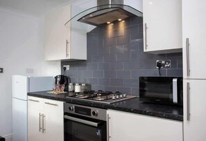 A modern kitchen with white cabinets, a gas stove, an oven, a microwave, and a stainless steel range hood.