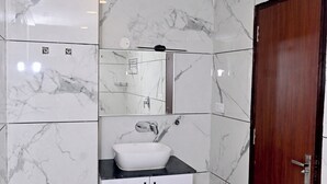 Een badkamer met witte marmeren tegels, een witte wasbak en een houten deur.