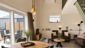 Un salon moderne avec une table ronde en bois, deux canapés, un téléviseur et une fenêtre donnant sur un immeuble en briques.