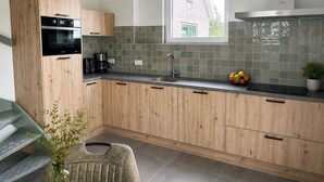 Une cuisine moderne avec des meubles en bois, un four encastré, une machine à café et une fenêtre.
