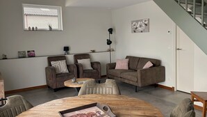 A modern living room with a sofa set, a dining table, and a staircase. - Luxury Hay Barn Holiday Home with Open Countryside Views in the Green Heart (Alphen aan den Rijn)