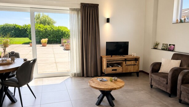 A modern living room with a TV, a wooden coffee table, a sofa, and a dining area with chairs. - Luxury Hay Barn Holiday Home with Open Countryside Views in the Green Heart (Alphen aan den Rijn)