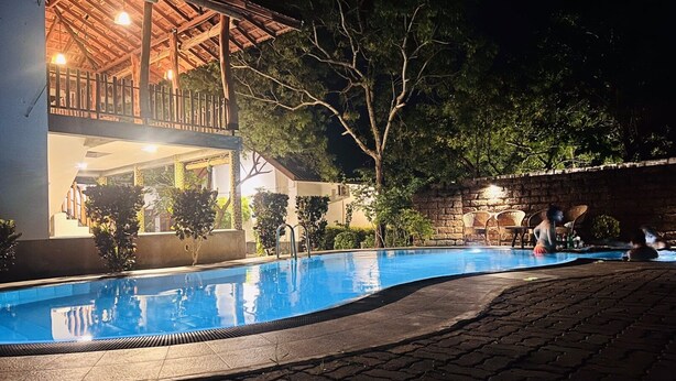 A swimming pool with a wooden deck and lounge chairs, surrounded by trees and a stone wall. - Yala Leopard Lodge (Kirinda)