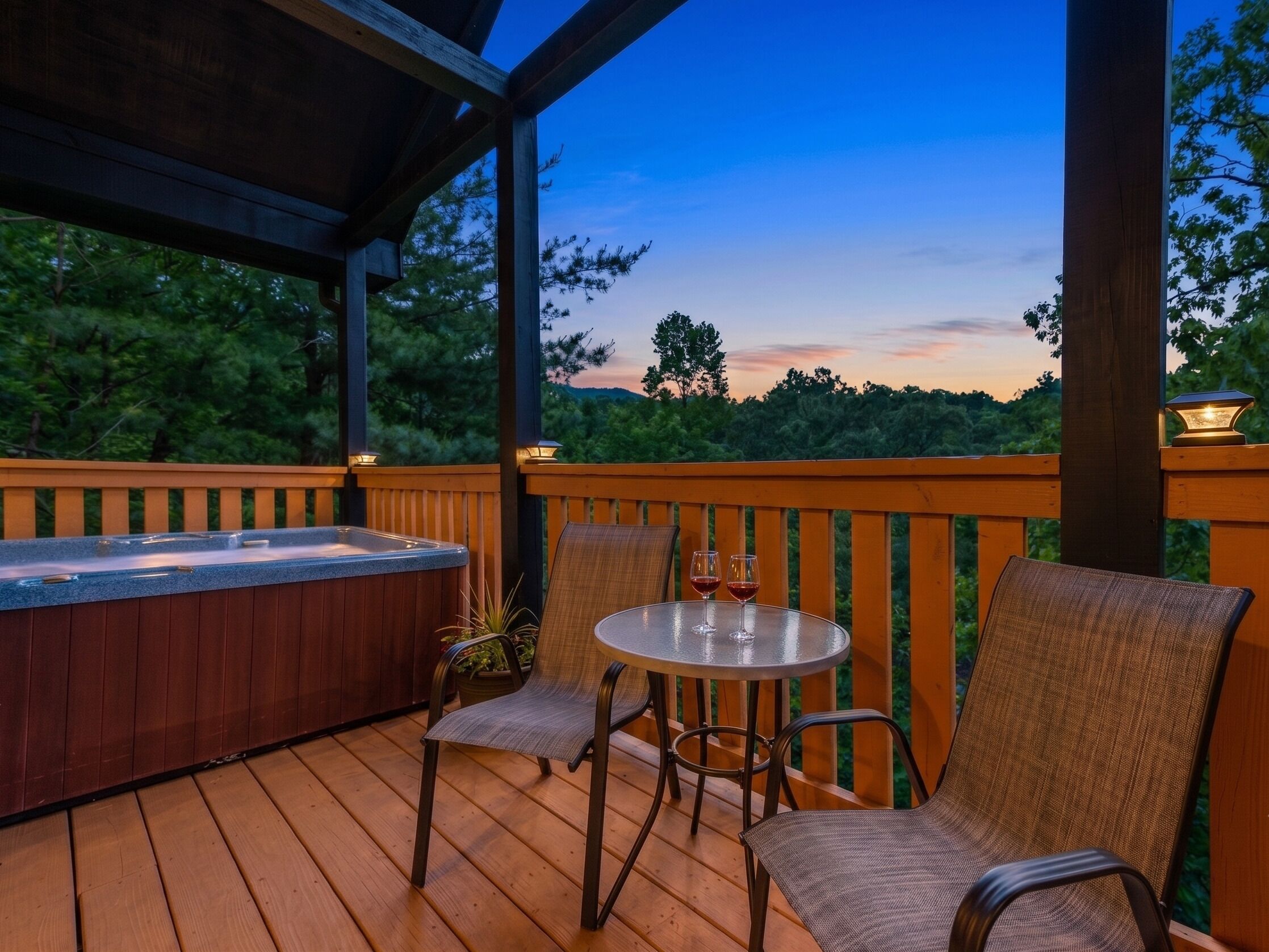 A wooden deck with a hot tub, two chairs, and a table with glasses.