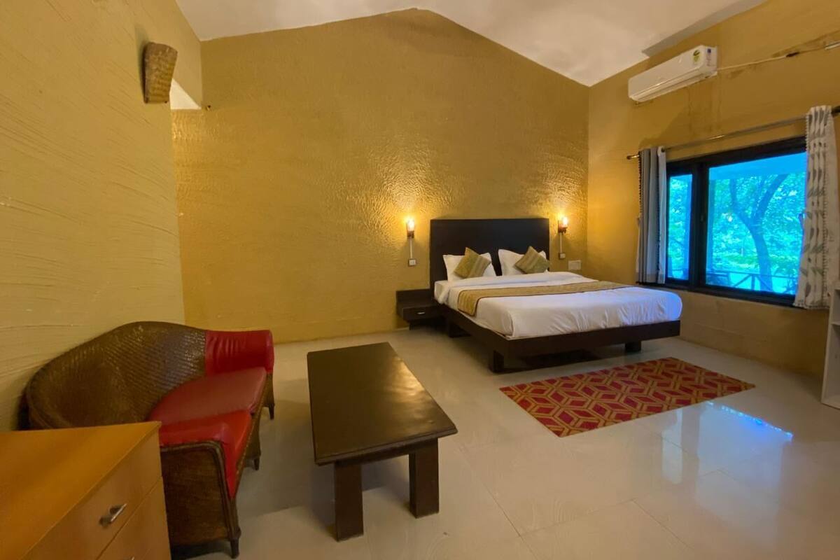 Una camera d'albergo con un letto, una panca in legno, un divano rosso e una finestra con tende.