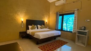A bedroom with a bed, bedside tables, a nightstand, a window with curtains, a ceiling fan, and a small table. - The Harikanta Corbett Resort (Marchula)
