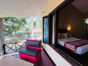 A room with a bed, a window, a balcony with a red chair, and a view of trees. - The Harikanta Corbett Resort (Marchula)