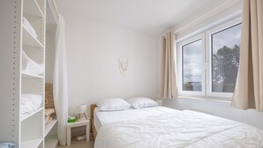 A bedroom with a bed, a wardrobe, a bedside table, and a window with curtains. - Ground Floor Apartment With Sunny Terrace (Middelkerke)