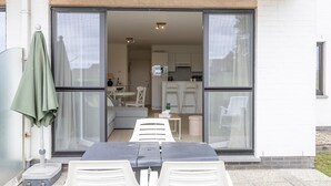 A patio with a table and chairs, a green umbrella, and a sliding glass door leading to a kitchen. - Ground Floor Apartment With Sunny Terrace (Middelkerke)