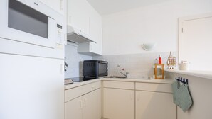 A compact kitchen with white cabinets, a microwave, a toaster, a sink, and a small countertop with a kettle and a ship decoration. - Ground Floor Apartment With Sunny Terrace (Middelkerke)